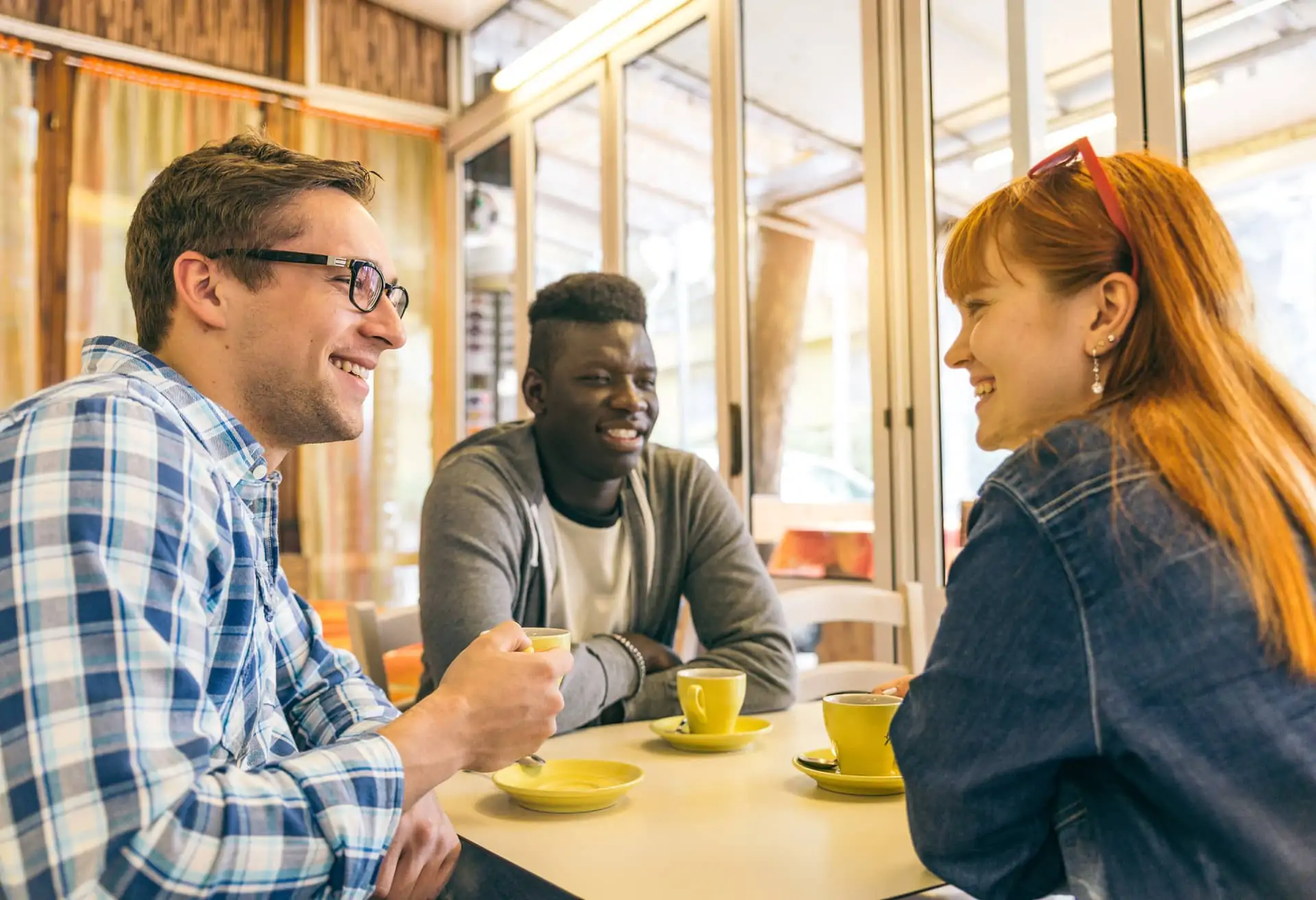 La imagen muestra un grupo de tres personas sentadas en una mesa. Están tomando café y teniendo una conversación.