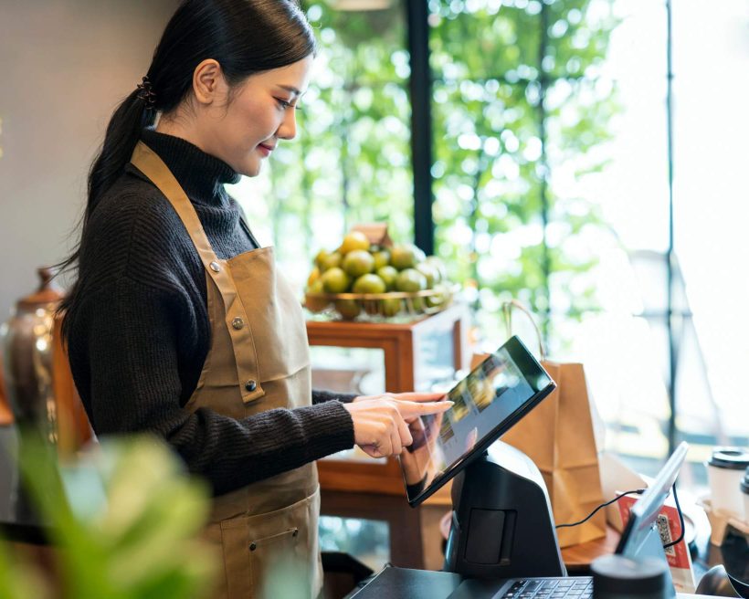 Imagen que muestra a una mujer con un suéter de cuello alto negro y un delantal café usando una tableta montada en un restaurante.