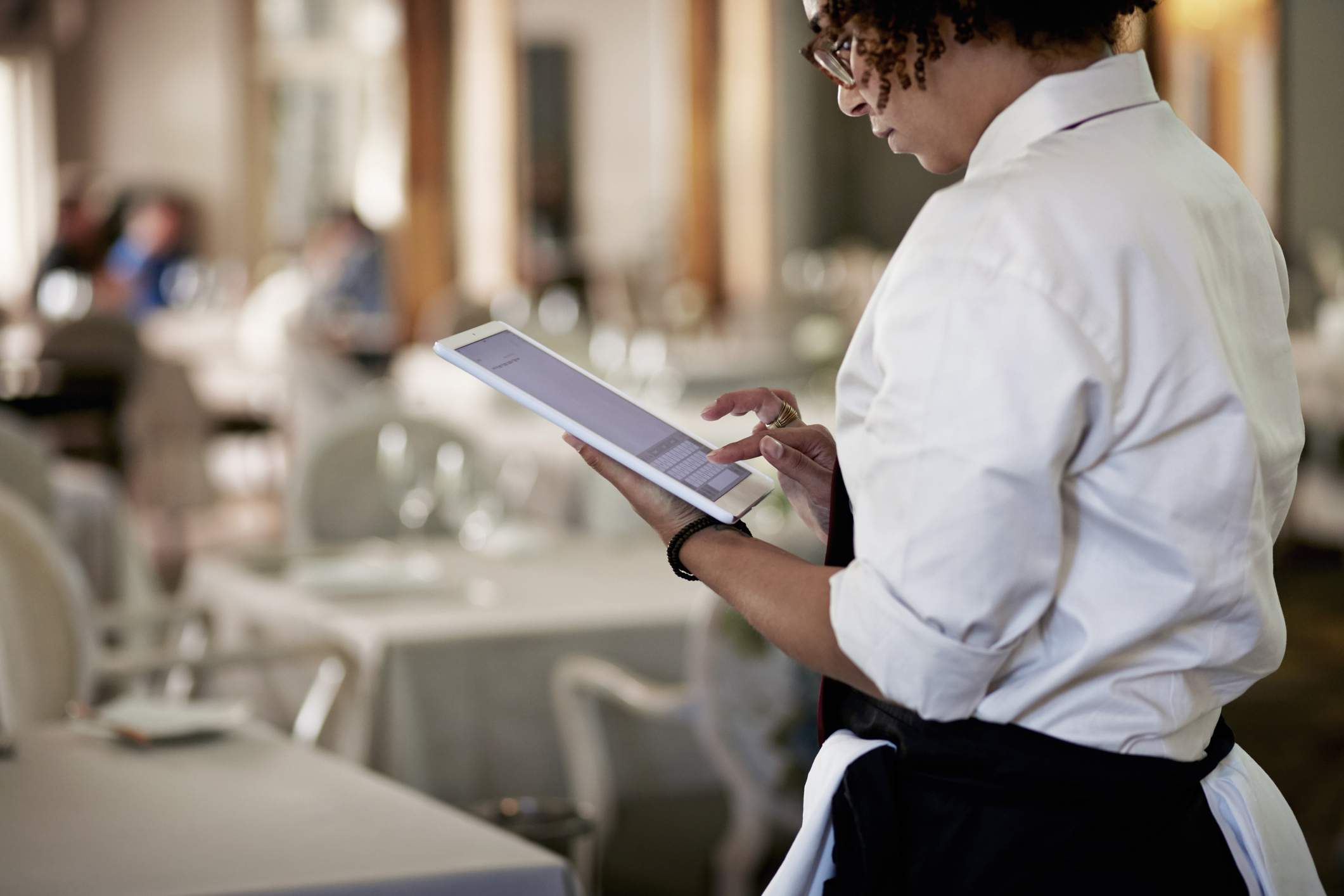 La imagen muestra a un mesero con una camisa blanca usando una tableta dentro de un restaurante