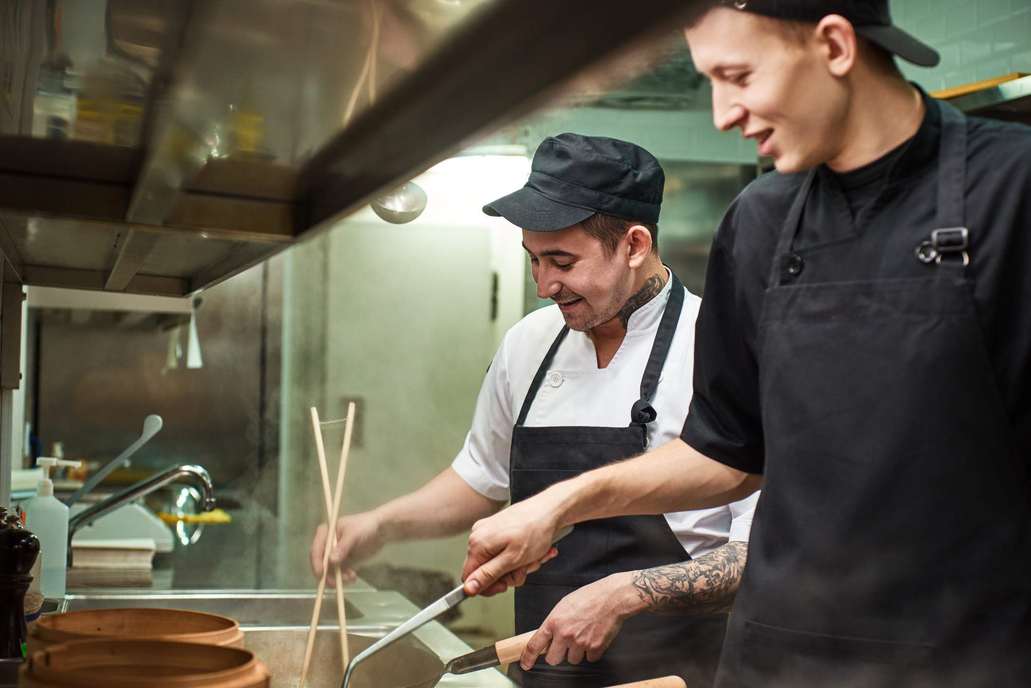 Esta imagen muestra la cocina de un restaurante donde dos chefs están preparando un plato. 