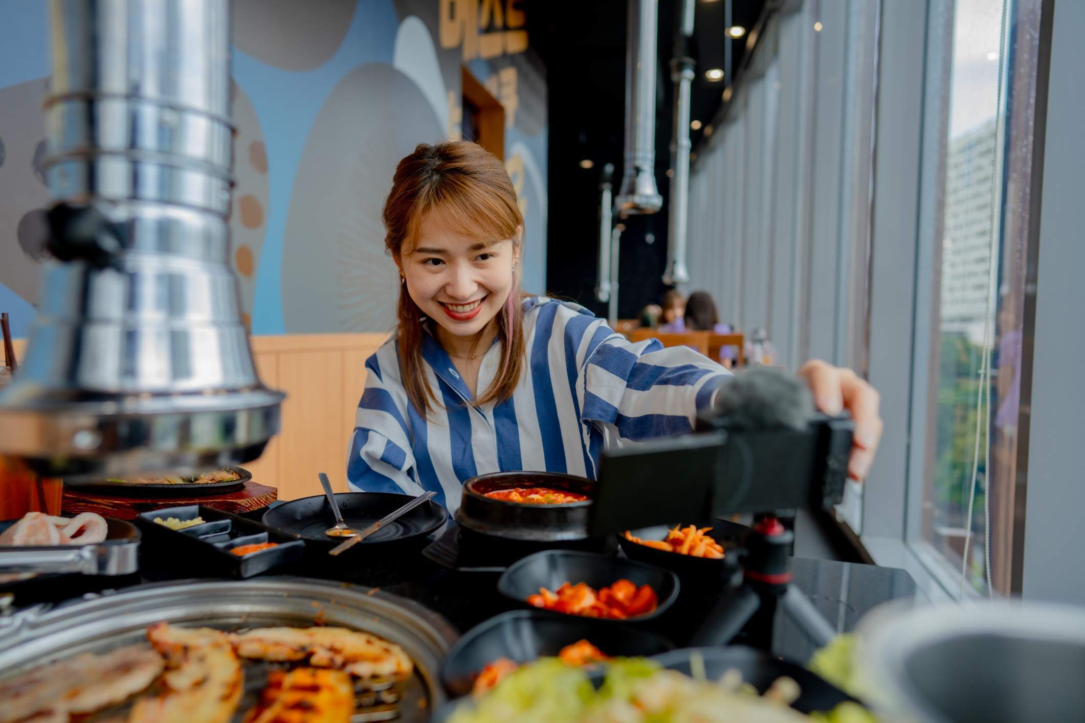 La imagen muestra a una comensal en un restaurante vlogueando su experiencia gastronómica. La mujer está colocando un teléfono sobre la mesa para grabar un video. 