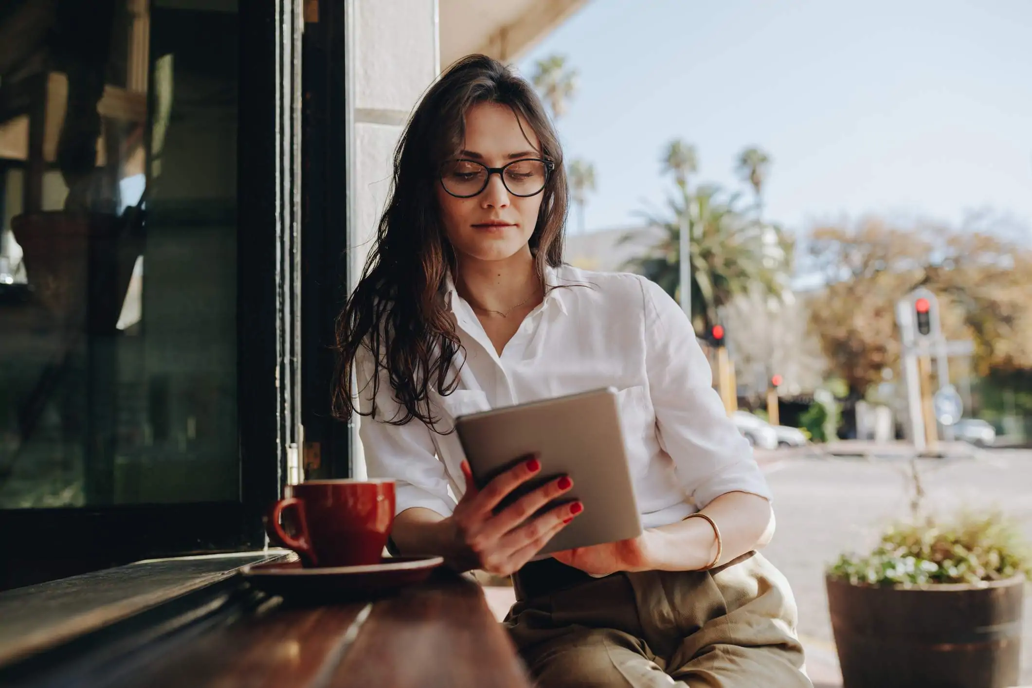 Mujer sentada en un café trabajando en una tableta digital. Mujer de negocios sentada en el mostrador de la cafetería con un café usando una tableta.